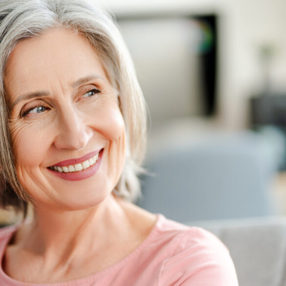 Smiling confident senior woman sitting on comfortable sofa at home. Happy female looking away