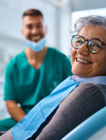 Happy woman at dental clinic looking at camera. Her dentist is in the background.