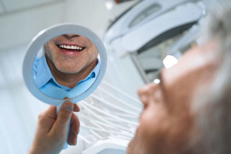 Jolly man is looking at mirror and enjoying reflectiong of his smile after dental implants