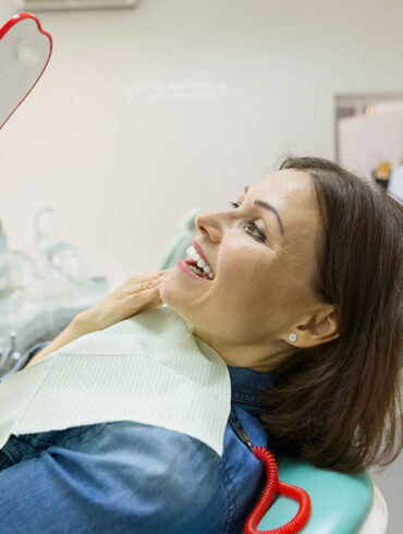 Woman patient looking in the mirror at the teeth, sitting in the dental chair