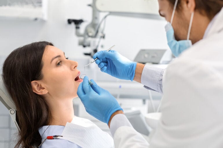 Young woman having regular check up in newest dental office, male dentist in gloves and mask holding dental tools, free space